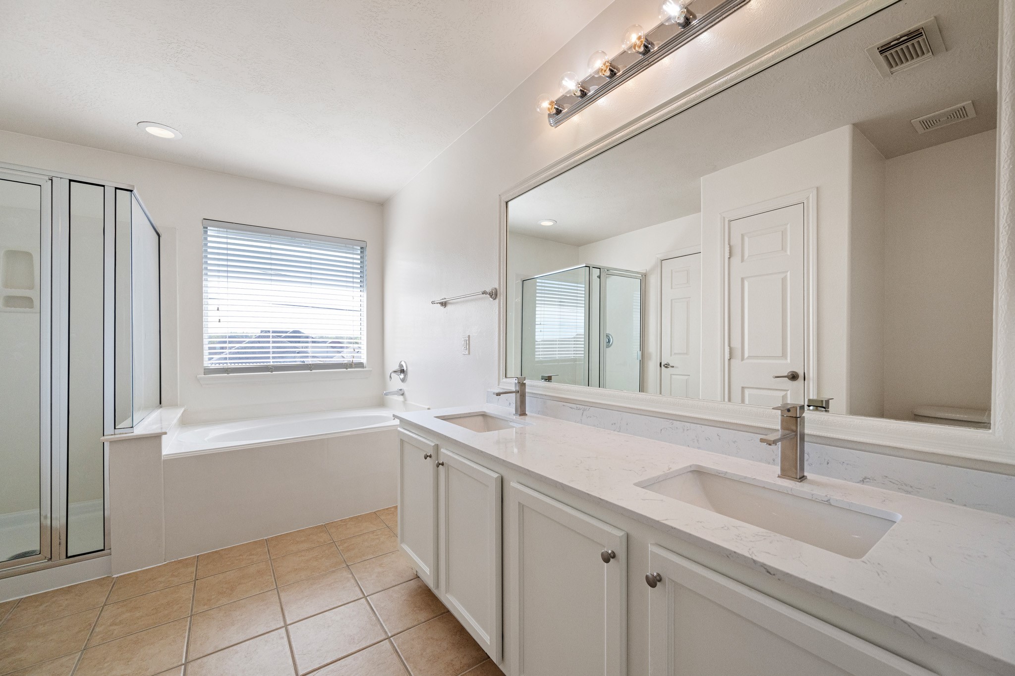 11938 Ramla Place Trail Houston, TX 77089 - Photo 19 of 28 This spacious primary bathroom offers a serene retreat with its elegant double vanity, sleek modern fixtures, expansive mirror, and a luxurious soaking tub complemented by a separate glass-enclosed shower, all bathed in natural light.