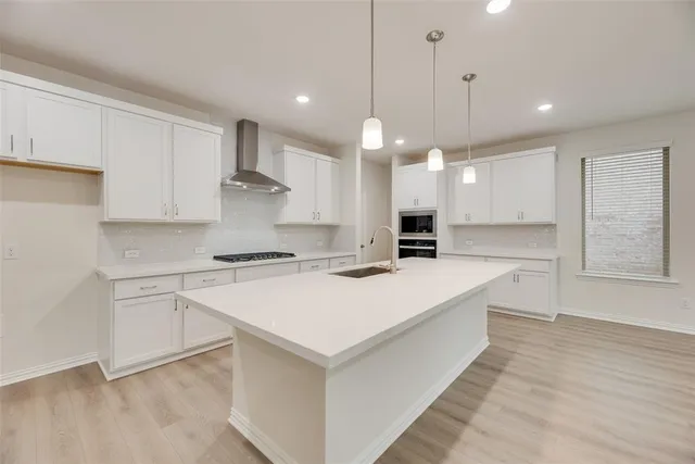 a large white kitchen with a large counter top space a sink stainless steel appliances and cabinets