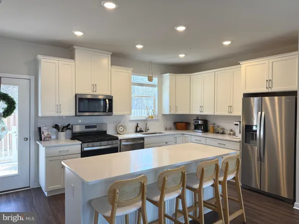 a kitchen with stainless steel appliances granite countertop a stove a sink a microwave a refrigerator with white cabinets and wooden floor