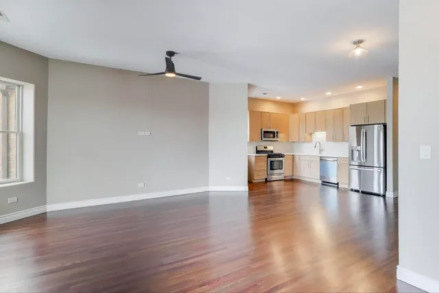 a view of an empty room and kitchen with wooden floor