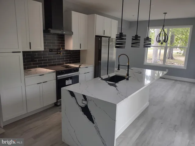 a kitchen with kitchen island granite countertop a stove a sink a refrigerator wooden floor and cabinets