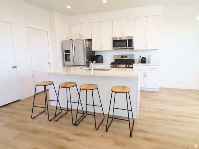 8240 Cascade Vw Way Magna, UT 84044 - Photo 3 of 18 Kitchen with stainless steel appliances, light wood-type flooring, a kitchen island with sink, white cabinets, and a kitchen bar