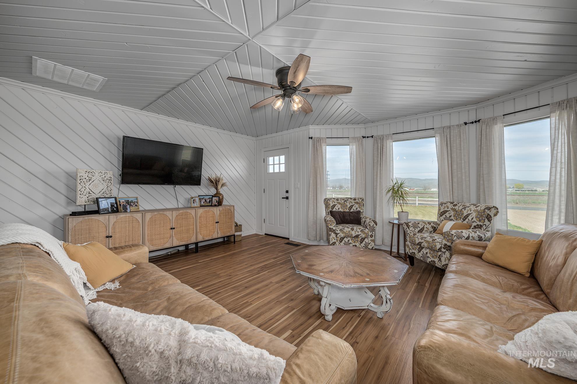 Living room featuring ceiling fan, wood finished floors, wood walls, and vaulted ceiling