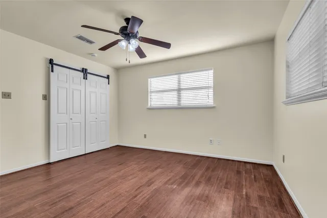 an empty room with wooden floor ceiling fan and windows