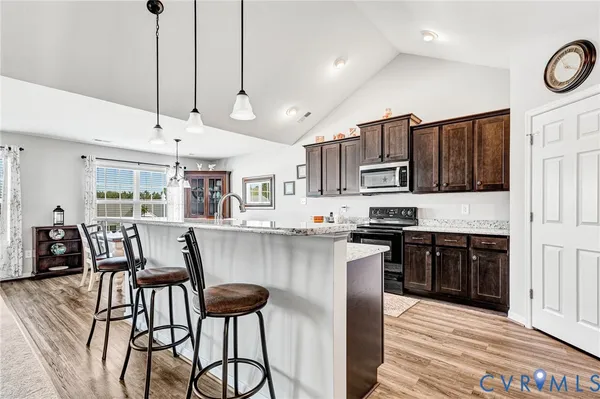 a kitchen with stainless steel appliances granite countertop a stove top oven a sink a dining table and chairs with wooden floor