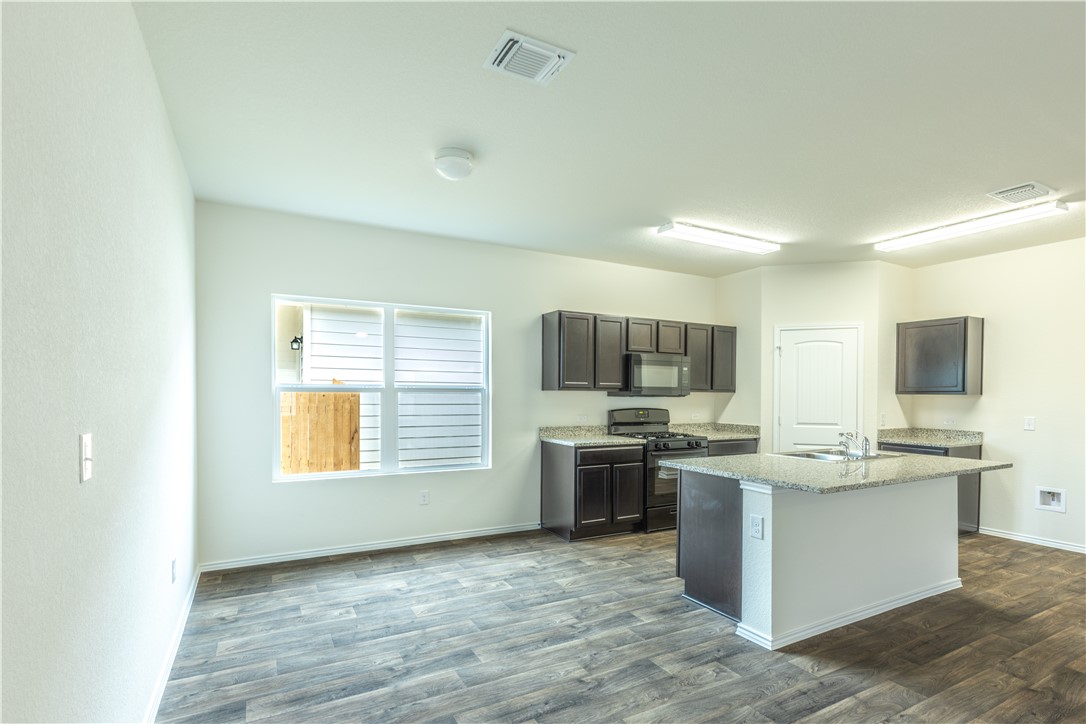 15204 Kent Justin Austin, TX 78725 - Photo 5 of 22 a kitchen with stainless steel appliances granite countertop a stove top oven a sink dishwasher a refrigerator and a dining table with wooden floor