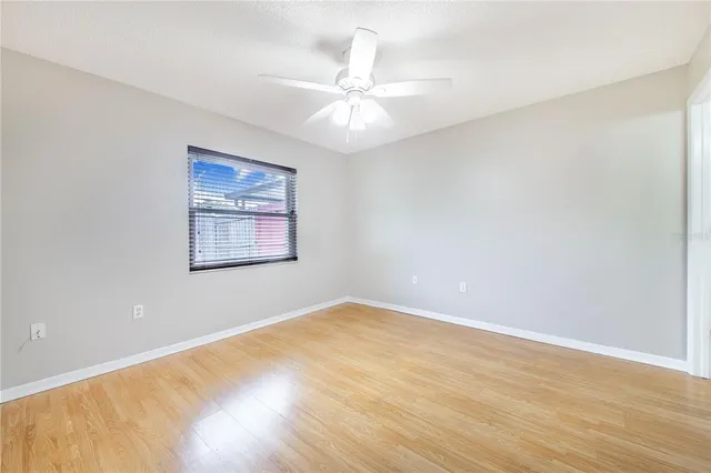 an empty room with wooden floor ceiling fan and windows