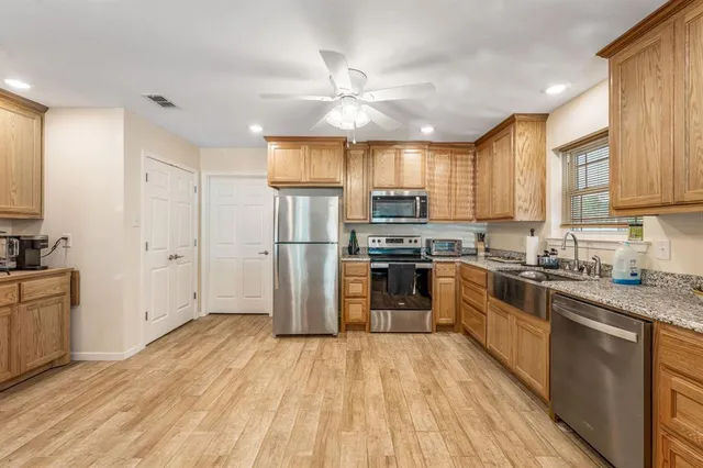 a kitchen with granite countertop a refrigerator oven a sink dishwasher and white cabinets with wooden floor