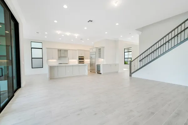 a view of an empty room with wooden floor and a kitchen