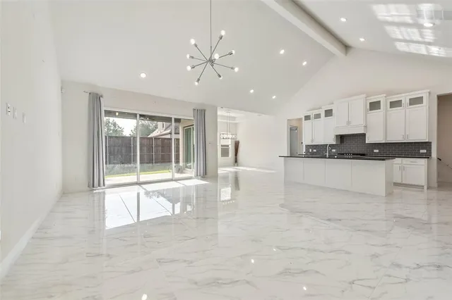 a large white kitchen with granite countertop a stove a sink a refrigerator and white cabinets with wooden floor