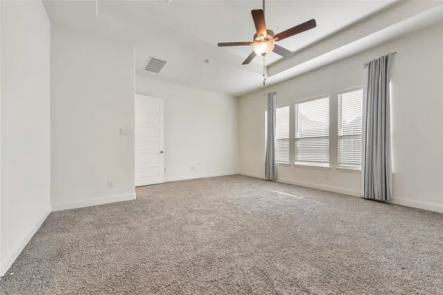 an empty room with chandelier fan and windows