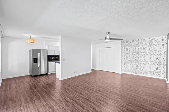 an empty room with wooden floor kitchen view and hallway