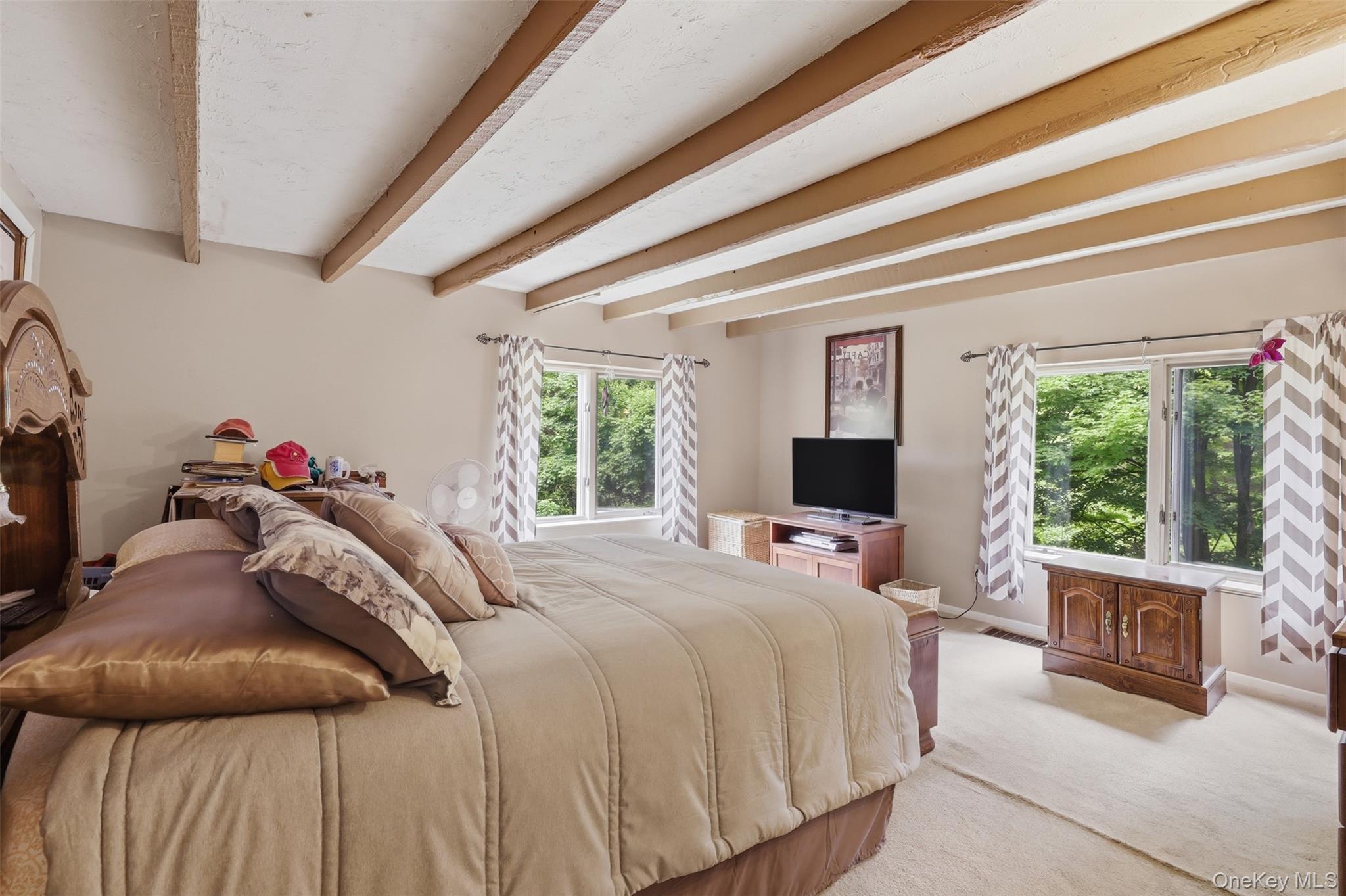 236 Hosner Mountain Road Hopewell Junction, NY 12533 - Photo 32 of 46 1st floor primary suite featuring exposed wood ceiling beams, neutral wall tones, and light-colored carpeting with closet on left side of bed and entrance to full bath on right side