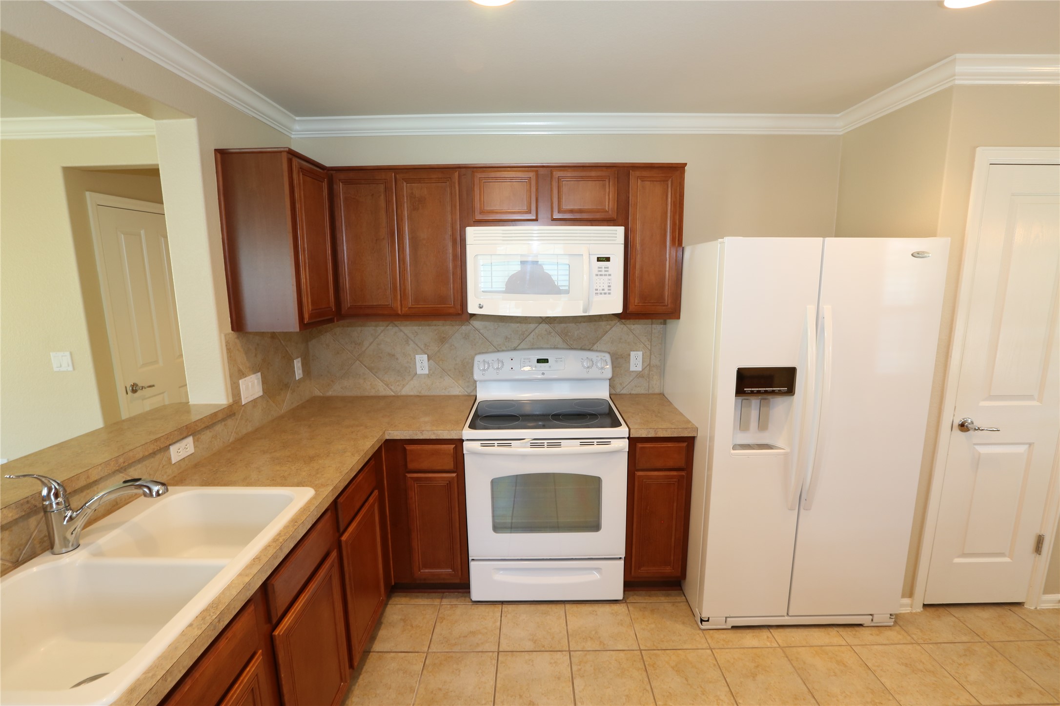 113 Monument Hill Trail Georgetown, TX 78633 - Photo 5 of 29 Kitchen with white appliances, light countertops, ornamental molding, brown cabinets, and tasteful backsplash