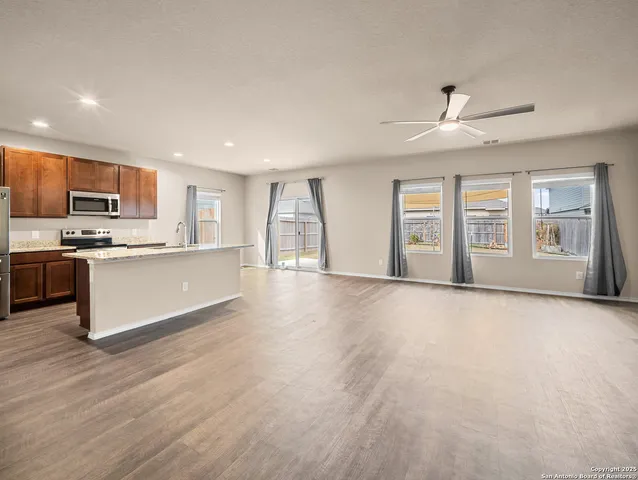 a living room with stainless steel appliances kitchen island granite countertop a stove a sink a refrigerator white cabinets and wooden floor