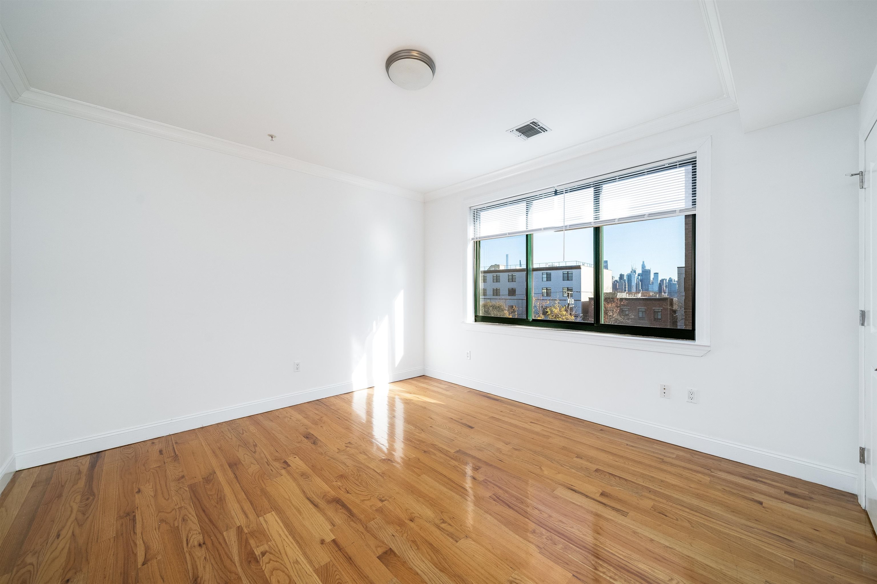 85 Maple Street, Unit 2L Weehawken, NJ 07086 - Photo 4 of 11 a view of an empty room with wooden floor and a window