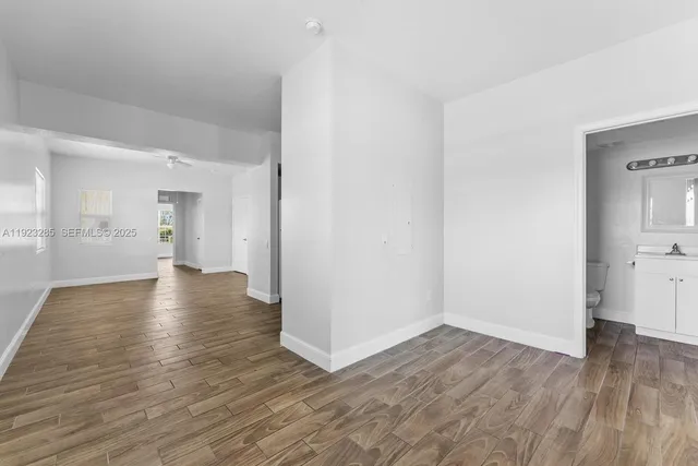 a view of an empty room with wooden floor and a bathroom