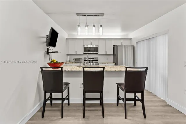 a kitchen with stainless steel appliances granite countertop a dining table chairs and a refrigerator