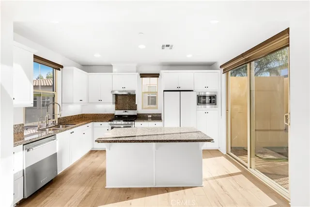 a large kitchen with stainless steel appliances a large counter top a stove a refrigerator and white cabinets
