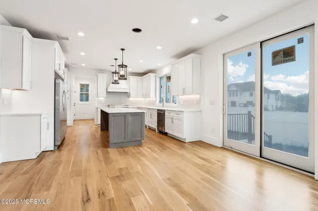 a large kitchen with stainless steel appliances kitchen island a stove a refrigerator a sink dishwasher and a living room with wooden floor