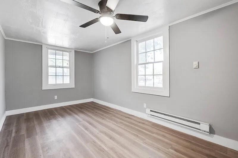 216 East Division Street Pilot Point, TX 76258 - Photo 12 of 17 Spacious room featuring wood-finish flooring, two large windows with white trim, contemporary gray wall paint, white baseboards, and a ceiling fan with integrated lighting