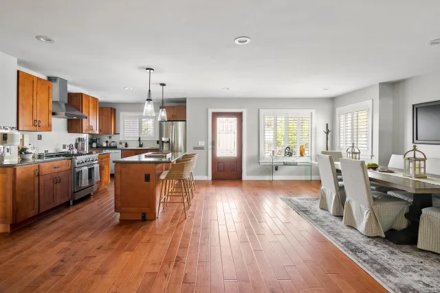 a kitchen with stainless steel appliances granite countertop a refrigerator a sink dishwasher a stove and a dining table with wooden floor