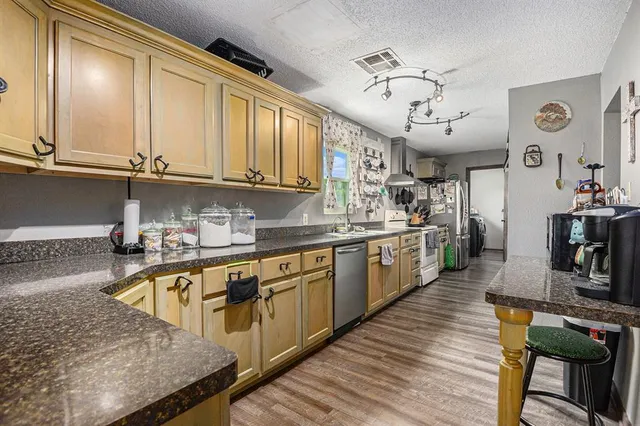 a kitchen with stainless steel appliances granite countertop a sink dishwasher stove and wooden cabinets with wooden floor