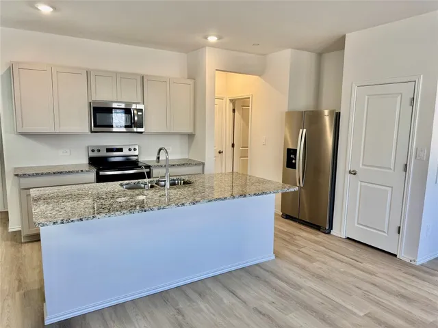 a kitchen with stainless steel appliances granite countertop a refrigerator a stove a sink and white cabinets with wooden floor