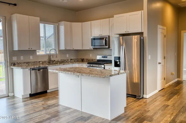 a kitchen with stainless steel appliances granite countertop a refrigerator a stove a sink and white cabinets