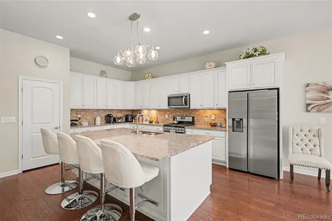 a kitchen with kitchen island granite countertop stainless steel appliances a refrigerator a stove cabinets dining table and chairs
