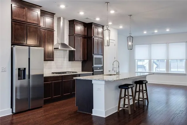 a kitchen with stainless steel appliances granite countertop a refrigerator a sink dishwasher a stove and a microwave oven on wooden floor