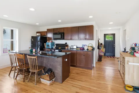 a kitchen with stainless steel appliances granite countertop a refrigerator a stove top oven and a dining table with wooden floor