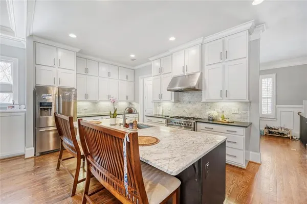 a kitchen with stainless steel appliances granite countertop a stove a refrigerator a sink a dining table and chairs with wooden floor