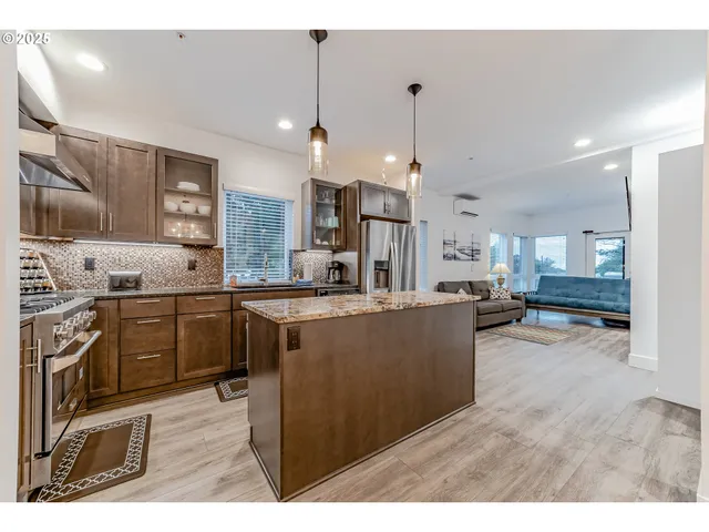 a kitchen with stainless steel appliances kitchen island granite countertop a refrigerator a stove a sink dishwasher and white cabinets with wooden floor