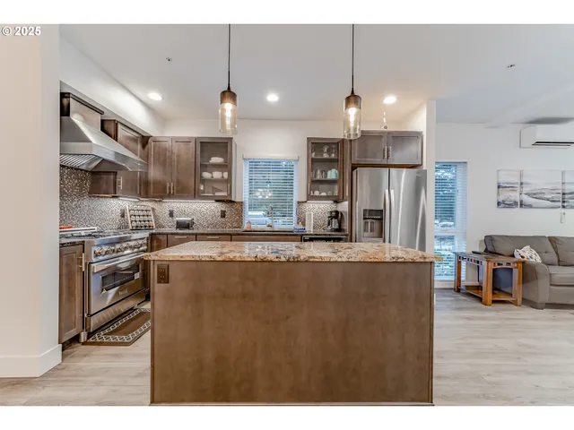 a kitchen with stainless steel appliances kitchen island granite countertop a refrigerator a stove a sink a oven and a dining table with wooden floor