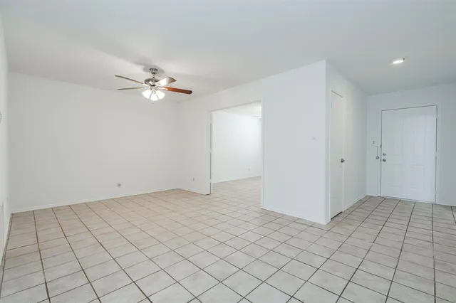 an empty room with white walls ceiling fan and window