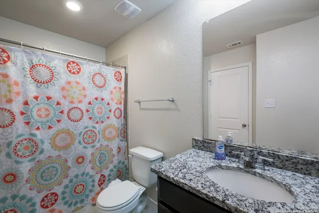 a bathroom with a granite countertop sink a toilet and a shower curtain