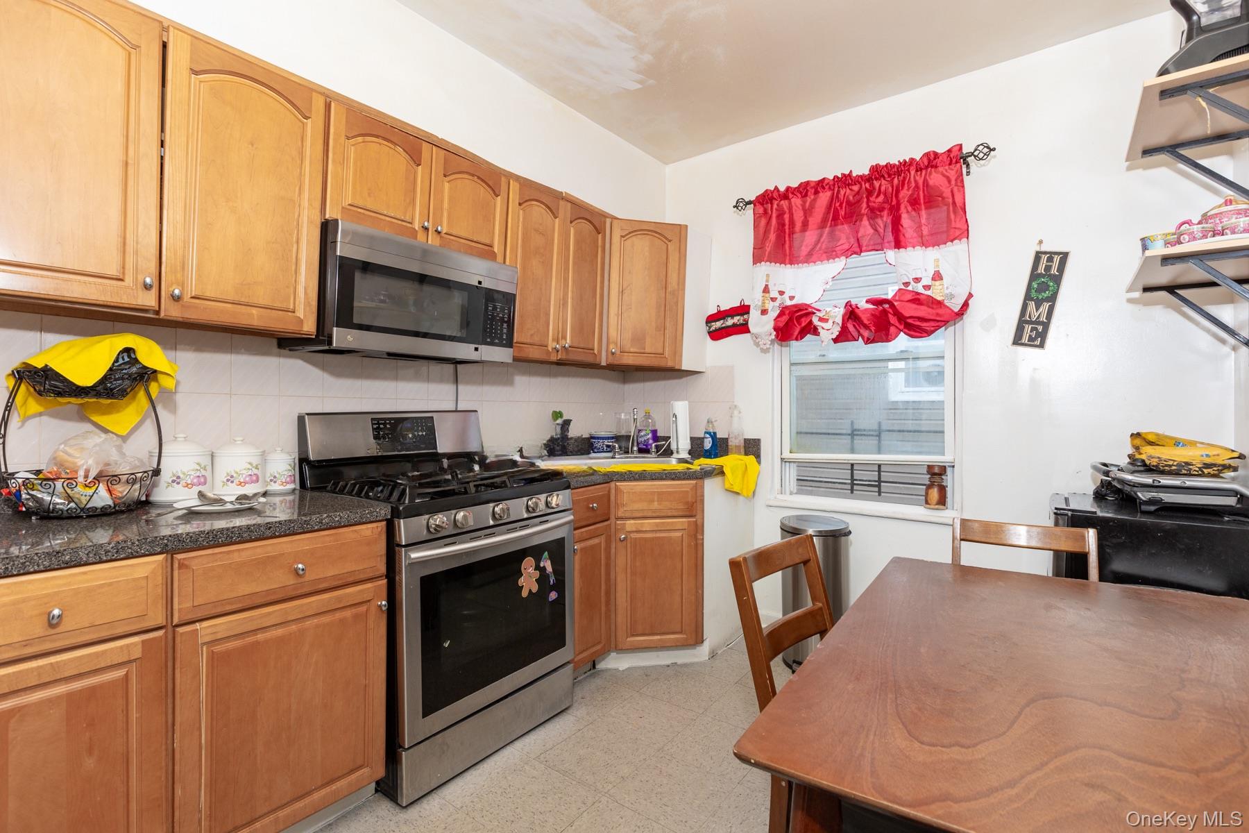 37-33 100th Street Queens, NY 11368 - Photo 12 of 14 Kitchen featuring stainless steel appliances, decorative backsplash, light floors, and brown cabinetry