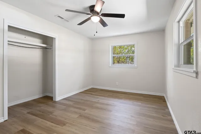 an empty room with wooden floor ceiling fan and windows