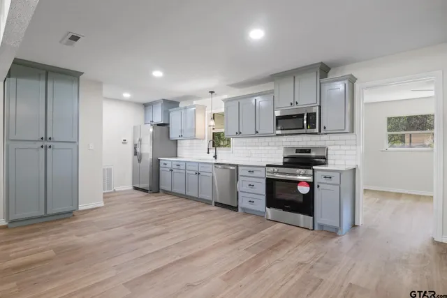 a kitchen with stainless steel appliances granite countertop a refrigerator a stove top oven a sink and dishwasher with wooden floor