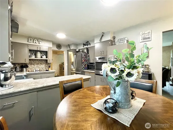 a living room with stainless steel appliances furniture a potted plant and a kitchen view