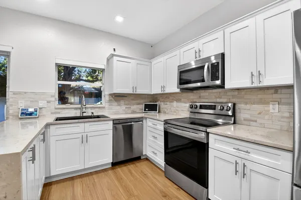 a kitchen with stainless steel appliances granite countertop white cabinets a sink a stove a microwave and wooden floors