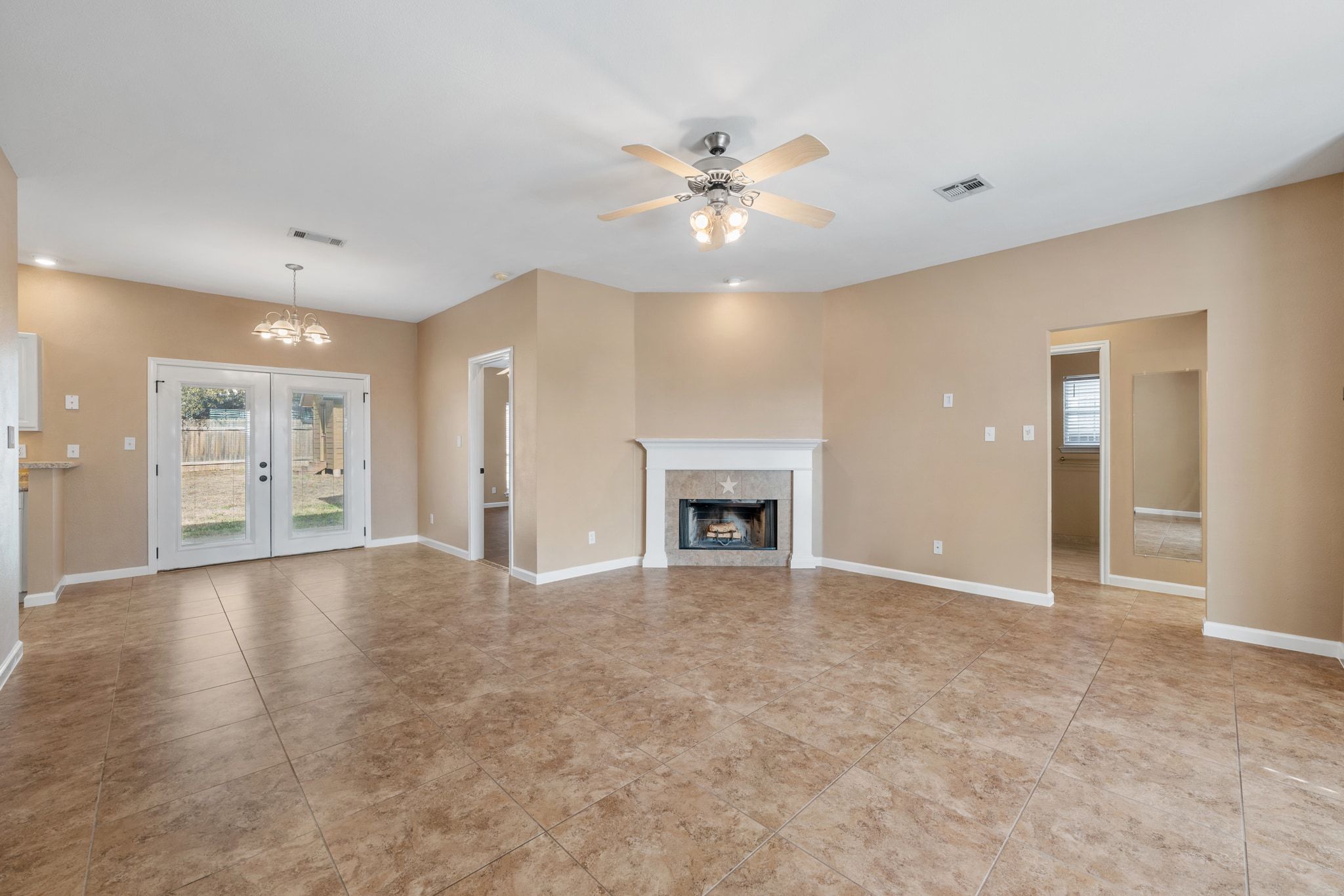 3139 Chisholm Trail Austin, TX 78734 - Photo 11 of 37 Unfurnished living room with a ceiling fan, hanging lights, french doors, a fireplace, and light tile patterned flooring
