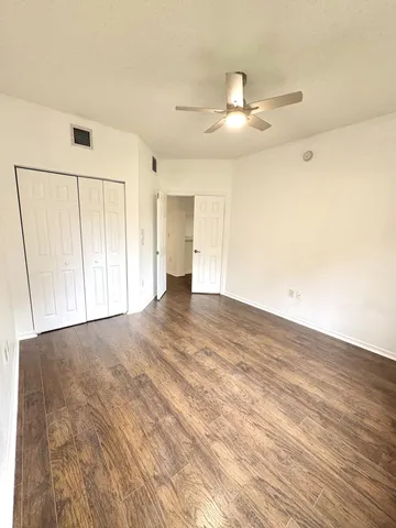 an empty room with wooden floor fan and windows