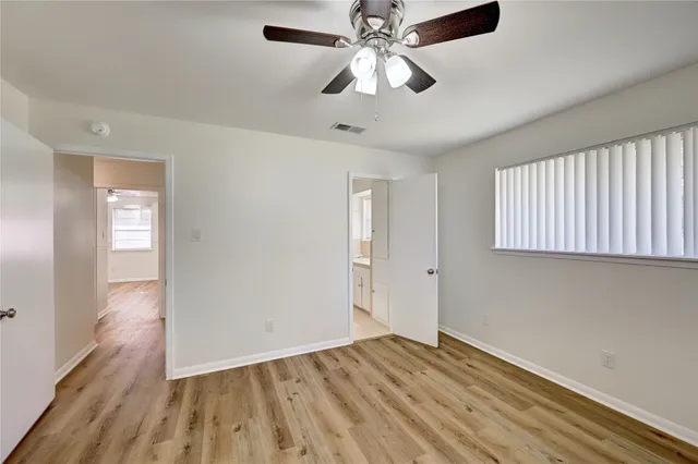 a view of an empty room with wooden floor and a ceiling fan