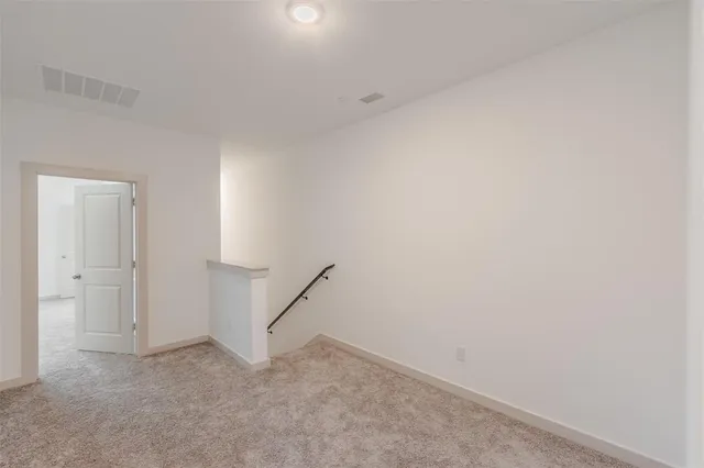 a view of an empty room with wooden floor and a kitchen