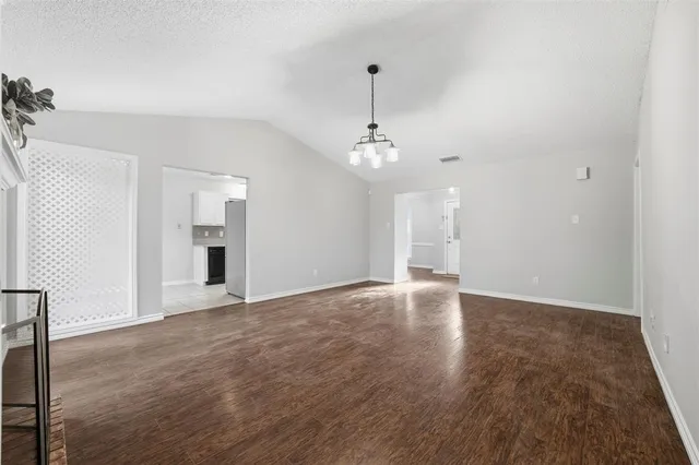a view of an empty room with chandelier and wooden floor
