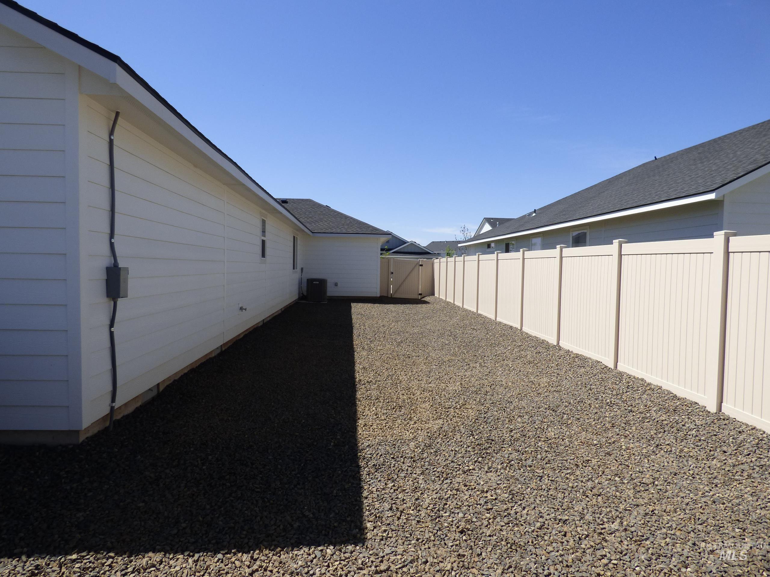 2708 East Buckaroo Drive Kuna, ID 83634 - Photo 46 of 48 Gravel side yard featuring a light-colored privacy fence with a matching gate, and a white siding exterior
