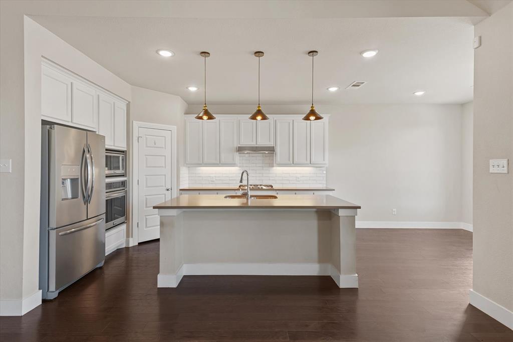 2044 Longbridge Road Forney, TX 75126 - Photo 8 of 40 Kitchen featuring white cabinetry, stainless steel appliances, a center island with sink, subway tile backsplash, and dark wood-finish flooring