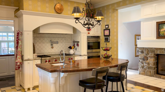 426 West Center Street Parowan, UT 84761 - Photo 23 of 107 Gourmet kitchen featuring a large central island with a polished countertop and seating, professional-grade range with pot filler, custom range hood, double wall ovens, and a stone fireplace surround